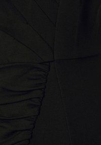 Gros plan sur un tissu noir avec des détails froncés et plissés créant des motifs texturés et géométriques.