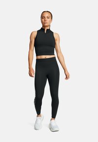 Svart prestationscrop top med hög hals, kombinerad med åtsittande svarta leggings med sidografiska detaljer och vita sportskor.