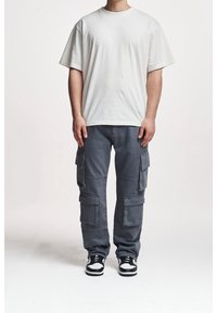 Bílá bavlněná trička kombinovaná se šedými cargo kalhotami s několika kapsami, rovný střih a černobílé tenisky.