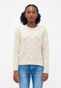 Šviesiai smėlinis megztinis, pasiūtas iš dygsniuotos nėriniais formos deimantų rašto, puošniai dekoruotas mažomis perlų detalėmis, su apvaliu kaklu ir įrėmintu rankogaliu.