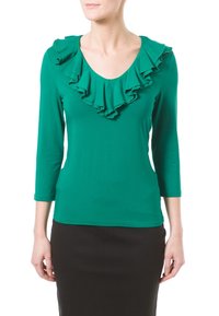 Grön långärmad topp med rundad halsringning och volangdetaljer runt kragen. Tillverkad av mjukt tyg, kombinerad med en svart kjol.