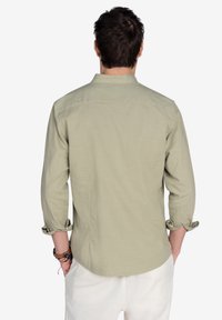 Camisa verde claro con las mangas arremangadas, un cuello y una tela texturizada. El diseño presenta un dobladillo recto y un corte relajado.