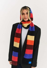 Dziany szalik z żywymi, poziomymi paskami w kolorach czerwonym, pomarańczowym, żółtym, czarnym, niebieskim i fioletowym, z małą niebieską metką.