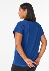 Mörkblå t-shirt med kort ärm i mjukt tyg, som har en avslappnad passform och rundad nederkant. Modellen har händerna knutna bakom ryggen.