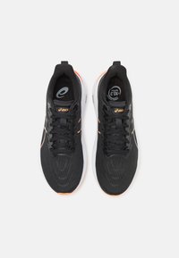 Black athletic shoes with orange accents, textile upper, laces, cushioned sole, and logo on tongue. Features geometric texture on surface.
