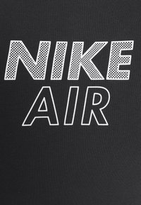 Svart tyg med vit text "NIKE AIR"; "NIKE" har ett fyllmönster i mesh, "AIR" är konturerad i vitt.