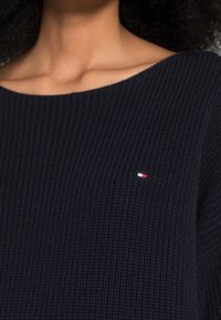 Námořnický pletený svetr s širokým výstřihem, na hrudi s malým červeným, bílým a modrým logem. Texturovaná tkanina a volný střih.