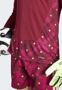 Burgundska sportska majica s geometrijskim uzorkom u nijansama ružičaste i krem, s CLIMACOOL oznakom. U pratnji crno-bijele nogometne lopte.