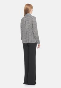 Blazer a righe bianco e nero con maniche lunghe, colletto a punta e una texture liscia, abbinato a pantaloni neri a gamba larga.