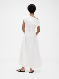 Hvit bomulls maxi-kjole med off-shoulder design, løs passform og vertikal sømdetalj. Brukt med svarte flip-flops.