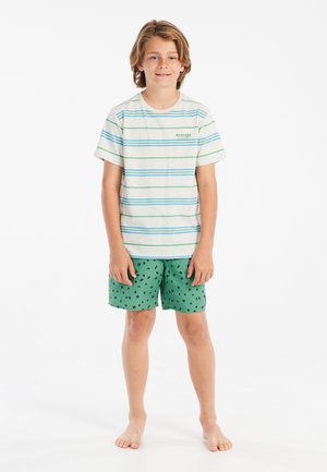 Gestreepte T-shirt met korte mouwen in lichtgrijs met blauwe en groene strepen, gecombineerd met groene shorts met zwarte sterrenpatronen. Blootsvoets.