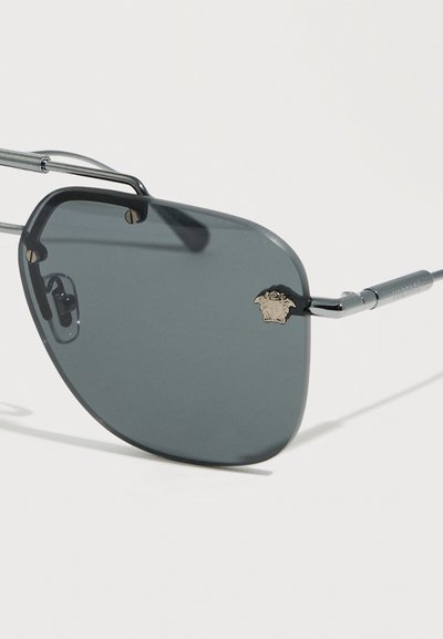 Γκρι ορθογώνιο φακός γυαλιών ηλίου με λεπτό ασημί μεταλλικό πλαίσιο και μικρή χρυσή λεπτομέρεια με το λογότυπο Medusa στην πάνω αριστερή γωνία.