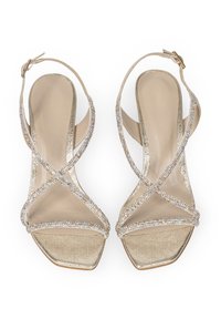 Złote sandały na obcasie z kwadratowym noskiem, ozdobione przezroczystymi akcentami z kryształków oraz teksturowaną wkładką. Regulowany pasek wokół kostki dla lepszego dopasowania.