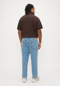 Καφέ κοντομάνικη μπλούζα, σε φαρδιά γραμμή, σε συνδυασμό με ανοιχτό μπλε φαρδιά τζιν παντελόνια που διαθέτουν πίσω τσέπες και ταμπά δερμάτινο έμπλαστρο στη μέση.