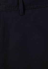 Tissu bleu marine foncé avec une texture lisse, présentant une couture et des passants de ceinture. Le matériau semble durable et étroitement tissé.