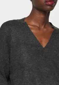Schwarzes V-Ausschnitt-Pullover in Anthrazit, mit gestrickter Textur, weichem Finish, entspannter Passform und rohen Kanten am Ausschnitt.