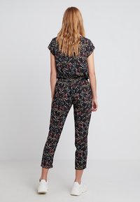 Svart blommig jumpsuit med korta ärmar, elastisk midja och avsmalnande ben. Har flerfärgade blommönster på en mörk bakgrund.
