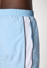 Pantalones cortos deportivos de color azul claro, hechos de un tejido suave, con un panel de malla blanca y un zipper lateral. Cintura elástica y detalle de ribete contrastante.