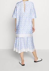 Abito blu chiaro con un motivo geometrico, maniche corte, chiusura sul retro con fiocco e gonna a strati. Tessuto liscio, lunghezza al ginocchio e vestibilità comoda.