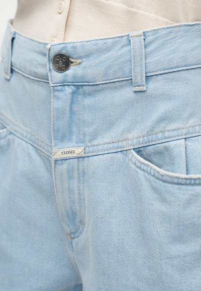 Ανοιχτό μπλε τζιν παντελόνι με κούμπωμα με κουμπιά, διακριτικό ράψιμο και ετικέτα με την επιγραφή "CLOSED" κοντά στην πίσω τσέπη.