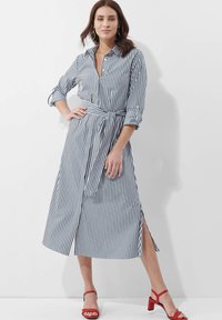 Gestreiftes Langarmkleid aus marineblau und weißem Stoff, mit Kragen, Knopfleiste, tailliertem Gürtel und Seitenschlitzen. Das Model trägt rote Sandalen.