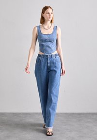 Plavi denim uskršeni top s strukturalnim šavovima, uparen s visokim, širokim plavim trapericama s rastrganim rubom. Srebrna lanac ogrlica.