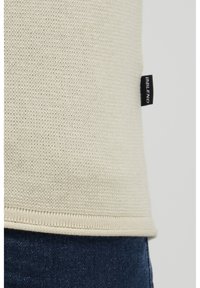 Beige strikket genser med en strukturert overflate, med en svart "BLEND"-etikett nederst og en rett nederkant. Jeans synlige nedenfor.