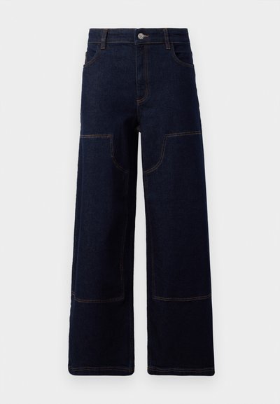 Calças de ganga largas, azul-escuras, com bolsos frontais e costura laranja em contraste, fecho com botão na cintura.