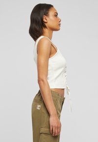 Vit kortärmad topp med snörning fram, parat med khaki cargobyxor med sidofickor och en broderad logotyp.