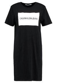 Černé šaty z bavlny s krátkým rukávem, na kterých je obdélníková bílá logo krabička s textem "CALVIN KLEIN JEANS" v šedé barvě.