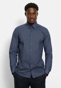 Marineblaues Hemd mit Knopfleiste und kleinem weißen geometrischen Muster, langen Ärmeln, spitzem Kragen und dunkelblauen Knöpfen. Taillierte Passform.