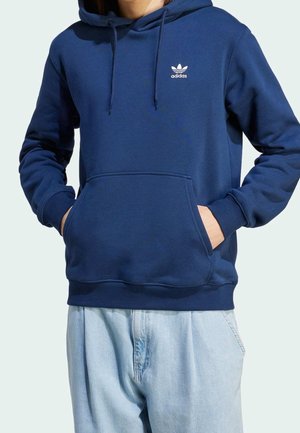 Tummansininen huppari, jossa on kengurupocket, nyörihuppu ja valkoinen Adidas-logo rinnassa; valmistettu pehmeästä, tekstuuripinnoitteisesta kankaasta.