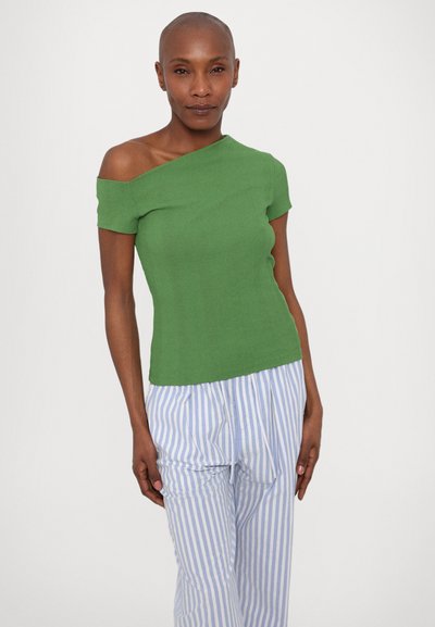 Tricou verde cu umerii descoperiți, realizat dintr-un material dublat, asortat cu pantaloni cu dungi albastre deschise. Tricoul are o formă ajustată și mâneci scurte.