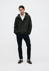 Fekete, könnyű dzseki kapucnival, két elülső zsebbel, fehér ing felett viselve. Sötét nadrág és fényes cipő teszi teljessé a megjelenést.