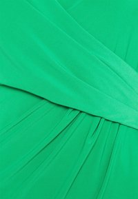 Zielona tkanina sukienkowa z marszczoną fakturą, charakteryzująca się gładkim opadaniem i ukośnymi fałdami. Materiał wygląda na miękki i lekki.