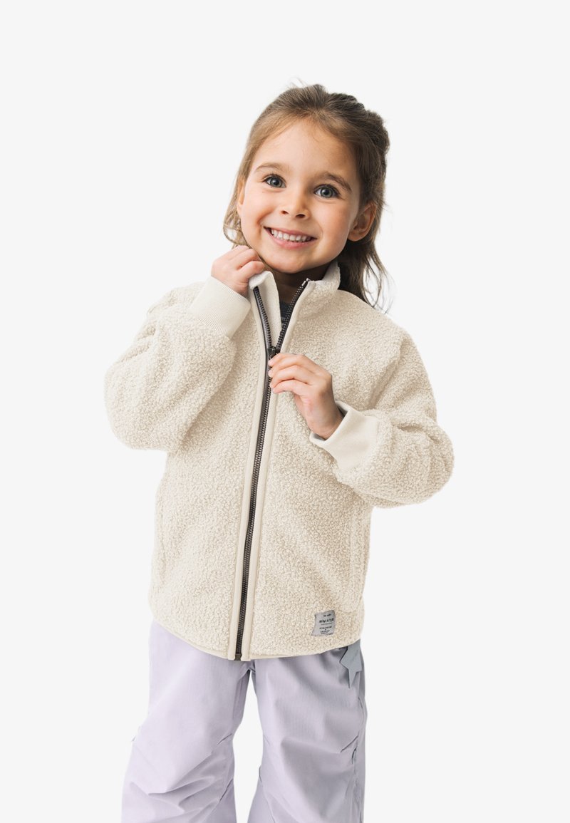 Fleecejacke in Creme mit strukturiertem Oberflächen, durchgehendem Reißverschluss und gerippten Bündchen. Tragen über einem dunklen Oberteil und hellen Hosen.
