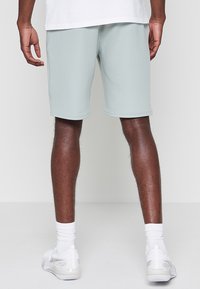 Pantaloni sportivi verde chiaro realizzati in tessuto liscio, con una vita elastica e un taglio fino al ginocchio. Indossati con scarpe sportive bianche e calze.