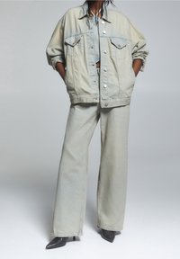 Chaqueta de mezclilla azul clara con dos bolsillos frontales, combinada con unos pantalones de pierna ancha a juego. Tejido texturizado con costuras y botones visibles.