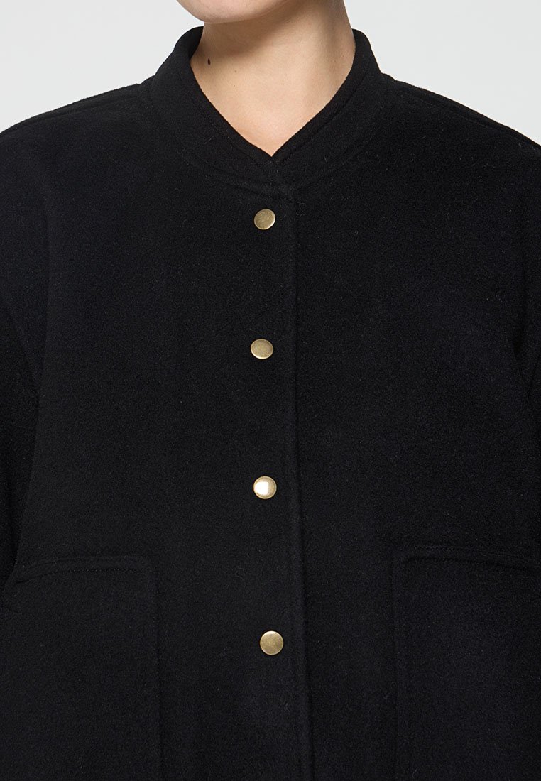 Schwarze Wollmischungjacke mit Kragen, ausgestattet mit goldfarbenen Druckknöpfen und zwei seitlichen Taschen. Weiche Textur, maßgeschneiderter Schnitt.