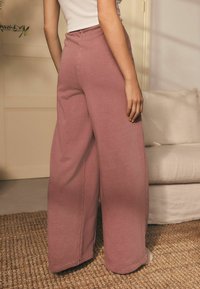Pantalones de pierna amplia de tela rosa suave, con cintura alta, textura suave y detalles de costura visibles, sobre un fondo neutro.