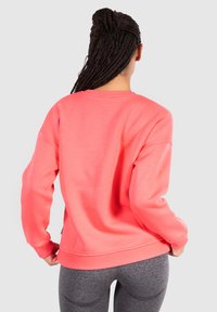 Korallfärgad sweatshirt med en avslappnad passform, ribbade ärmslut och fåll, som har mjukt tyg och minimala sömmar på baksidan.