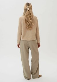 Beżowy wełniany sweter z okrągłym dołem i długimi rękawami, zestawiony z jasnobeżowymi spodniami typu wide-leg. Włosy upięte dużą klamrą.