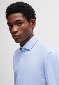 Lichtblauw overhemd met knopen, voorzien van een gestructureerde kraag en een subtiele textuurpatroon. Heeft witte knopen en een getailleerde pasvorm.