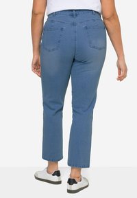 Vaqueros de mezclilla azules con una cintura alta, corte recto y dos bolsillos traseros. Combinados con zapatillas blancas con detalles en negro.