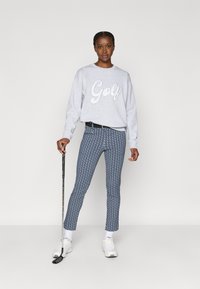 Pelēks sporta džemperis ar vārdu "Golf" baltām burtu krāsām, rakstainas zilas bikses, baltas kedas un rokās turēt golfa nūju.