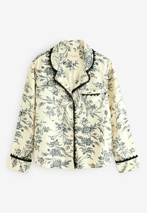 Floral-patterned pajama top in cream fabric with black accents, featuring button closure, a chest pocket, and contrasting black lace trim.