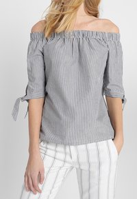 Off-the-shoulder topp i svart och vit vertikal rand. Har vida ärmar med knyt detaljer och en samlad halsringning. Mjuk, lättvikts tyg.