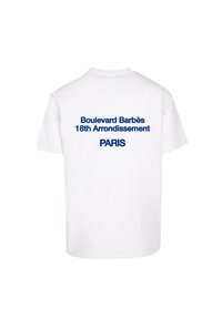 Camiseta blanca de algodón con texto azul en la parte posterior: "Boulevard Barbès 18º Arrondissement PARÍS." Cuello redondo estándar, mangas cortas.