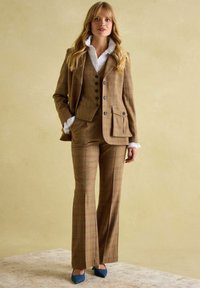 Hnedý károvaný oblek s priliehajúcou bundou a rozšírenými nohavicami. Obsahuje gombíky, vrecká a bielu volánovú košeľu pod ňou. Modré špicaté topánky.