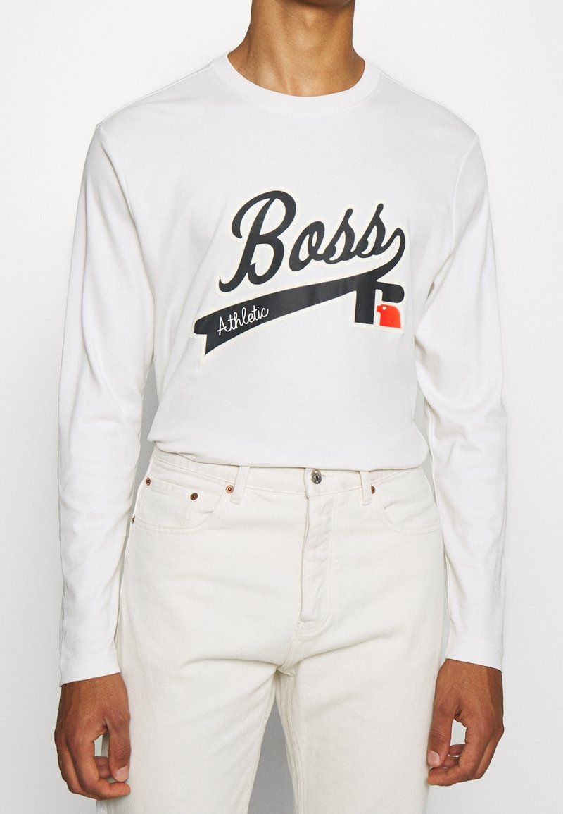 Vit långärmad skjorta med "Boss" tryckt i svart och röda accenter. Gjord av mjukt tyg, har rund halsringning och avslappnad passform.
